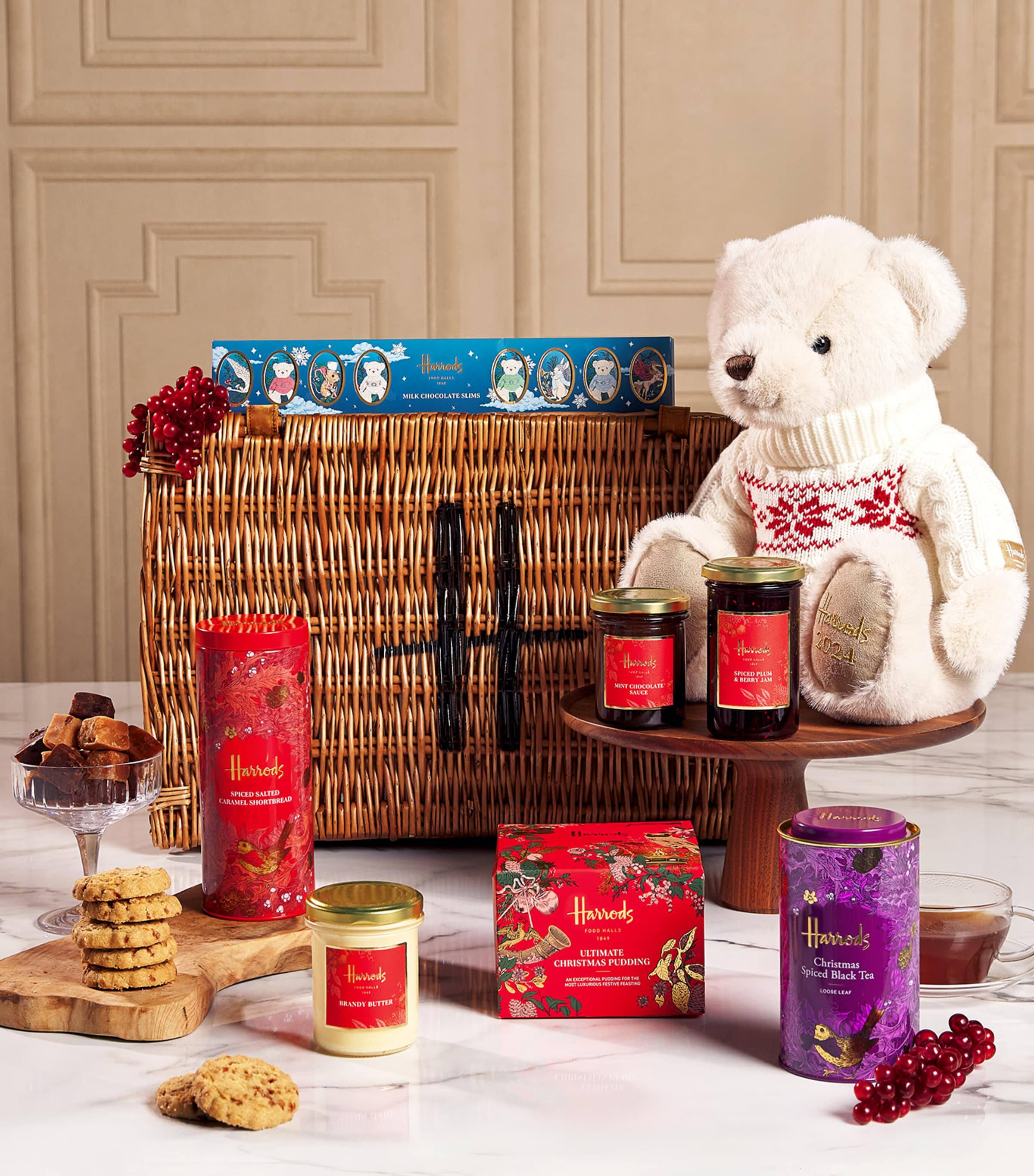 An open Harrods The Grosvenor Christmas hamper featuring sweet preserves, teas, chocolate, candles, and a teddy bear in a jumper
