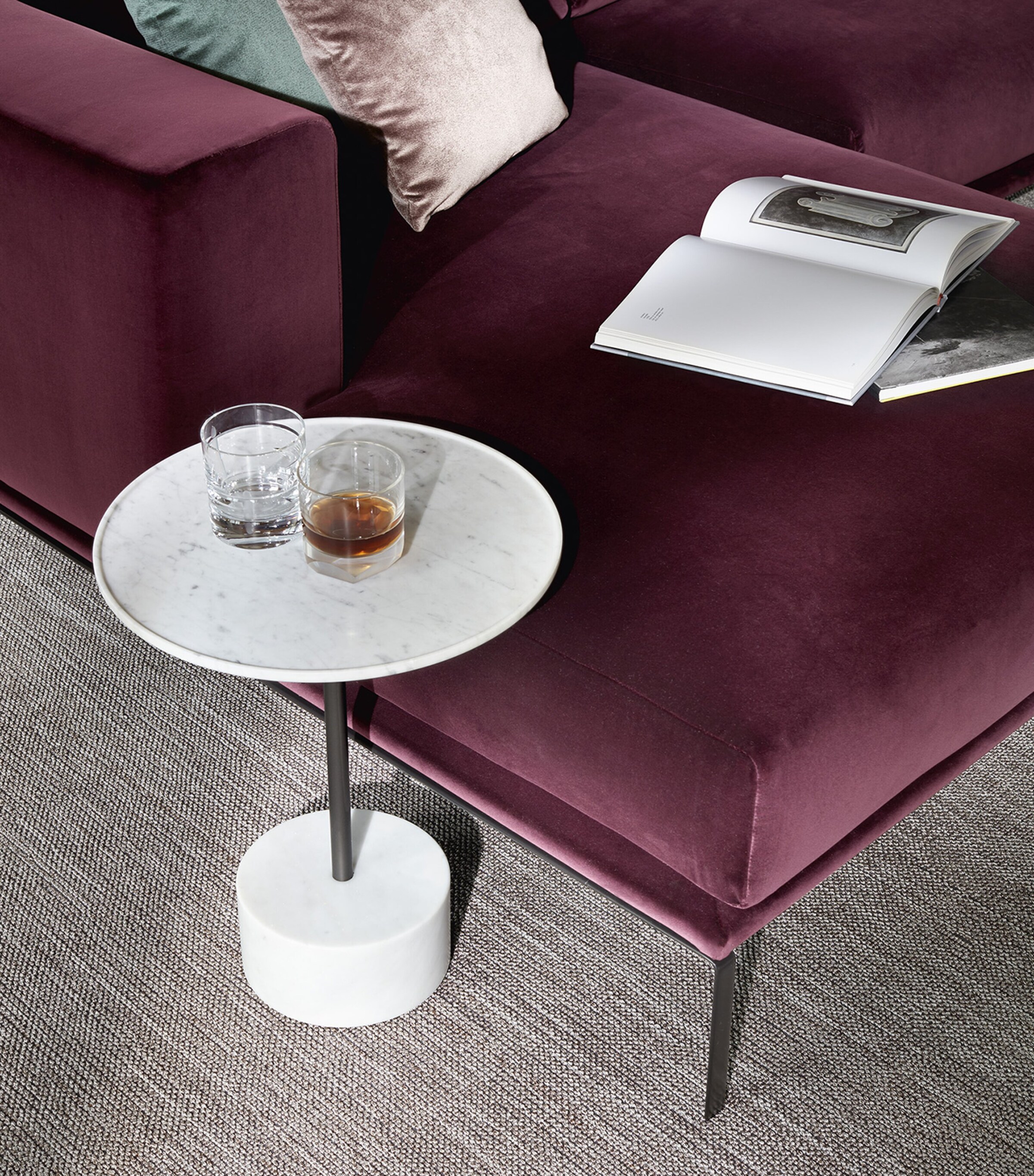 Marble round side table beside burgundy sofa with drink and book