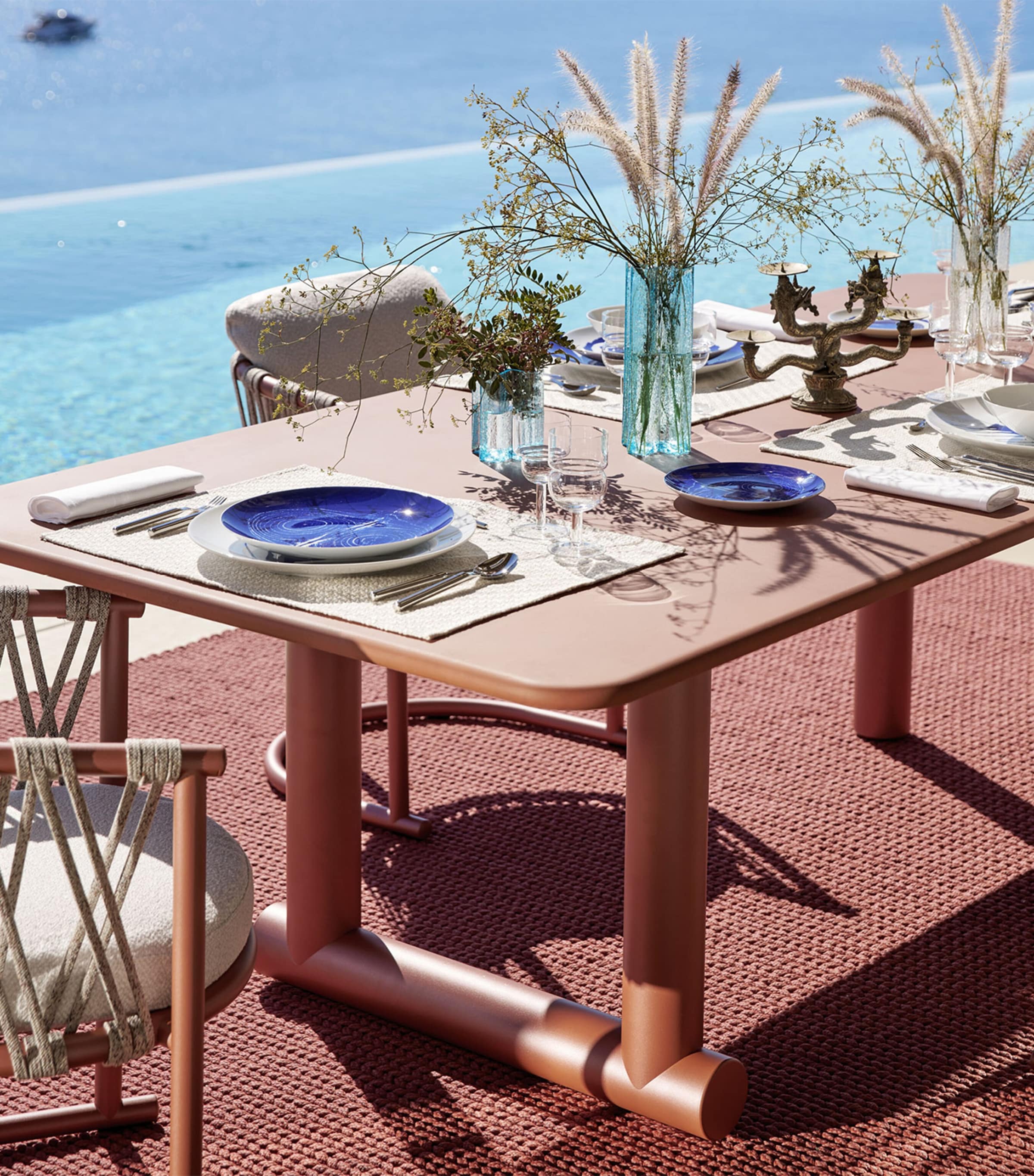 Brown dining table set with place settings on red outdoor rug
